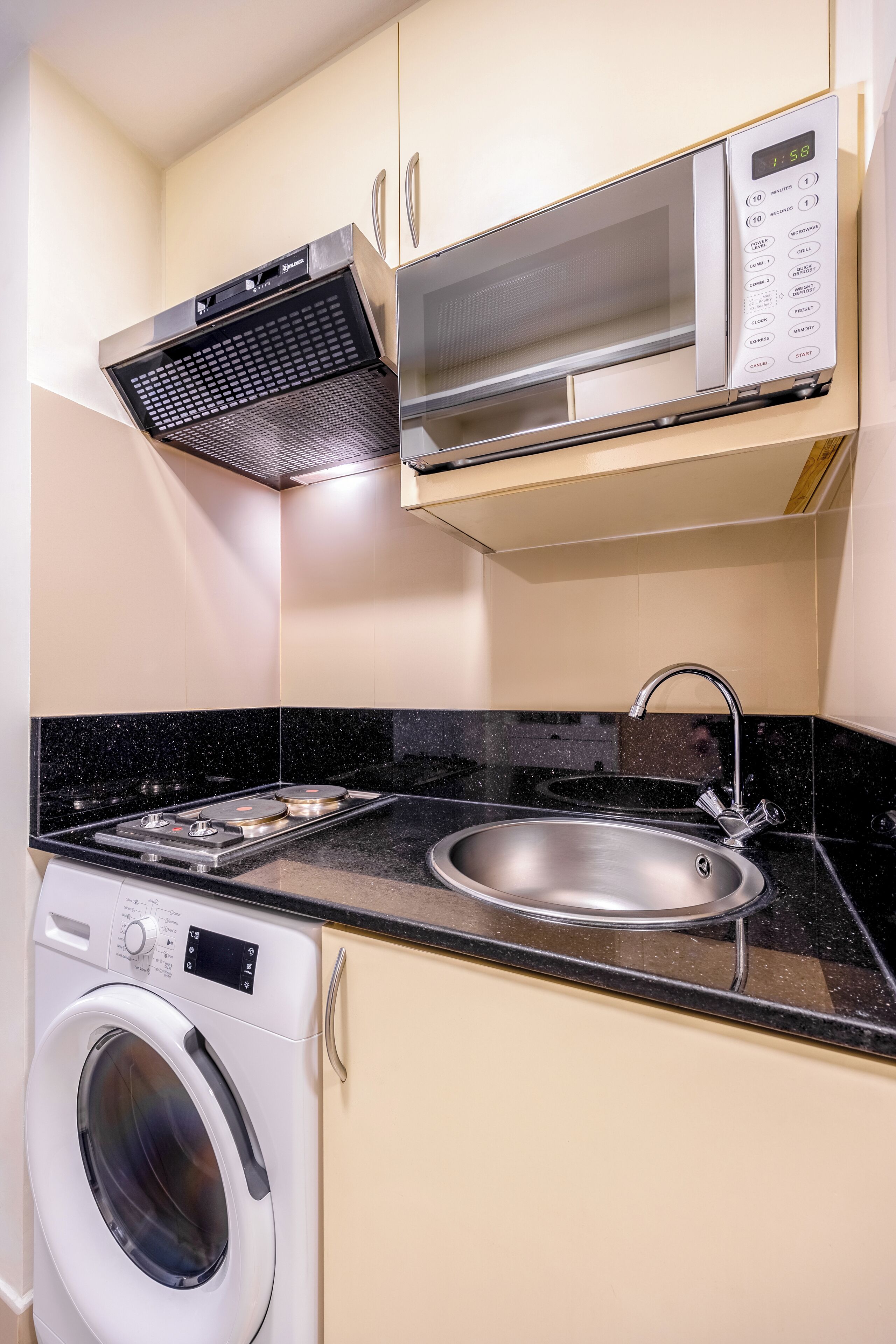 Una cucina compatta con forno a microonde, forno integrato, lavello e lavatrice.