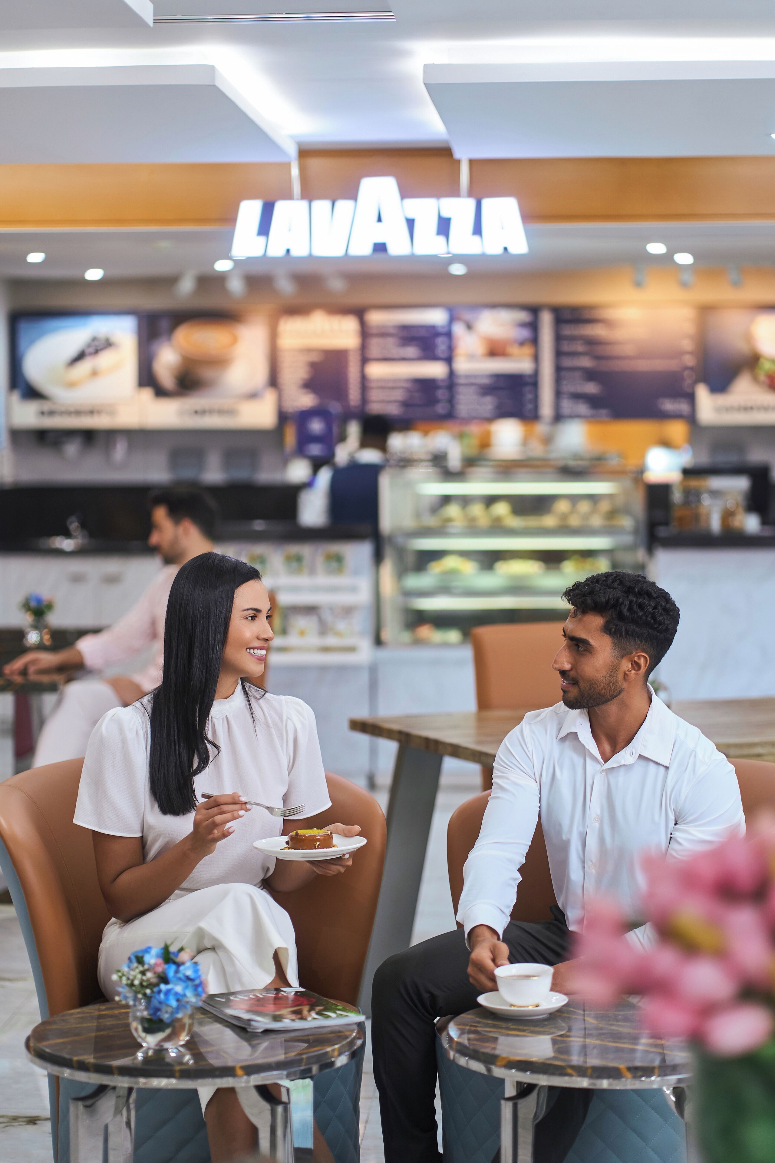Un couple est assis à une table dans un restaurant où l’on peut voir le menu affiché et une vitrine présentant les desserts.