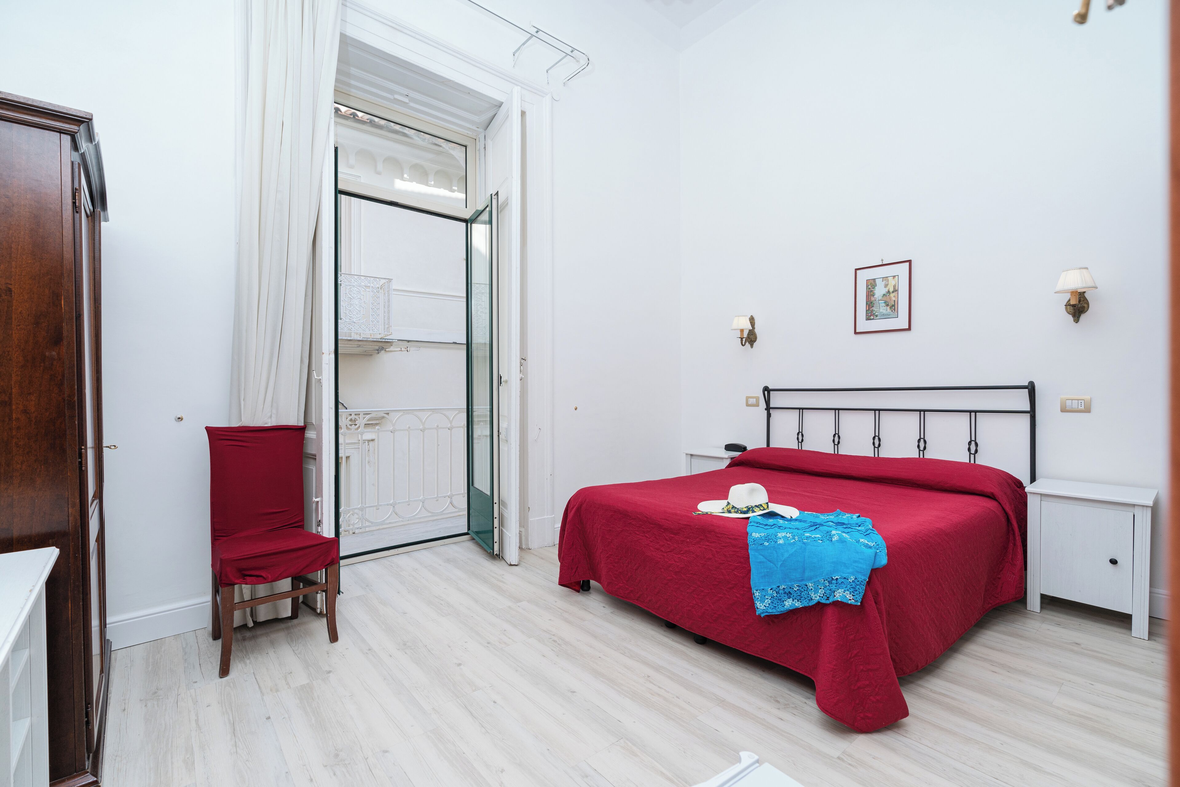 A bedroom with a bed, a chair, a door, and a wall-mounted light fixture.