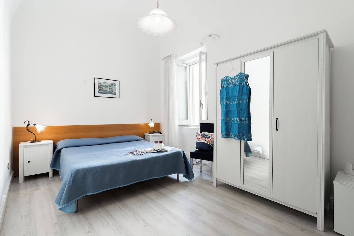 Ein Schlafzimmer mit Bett, Nachttischen, einem Kleiderschrank und einem Fenster mit Vorhängen.