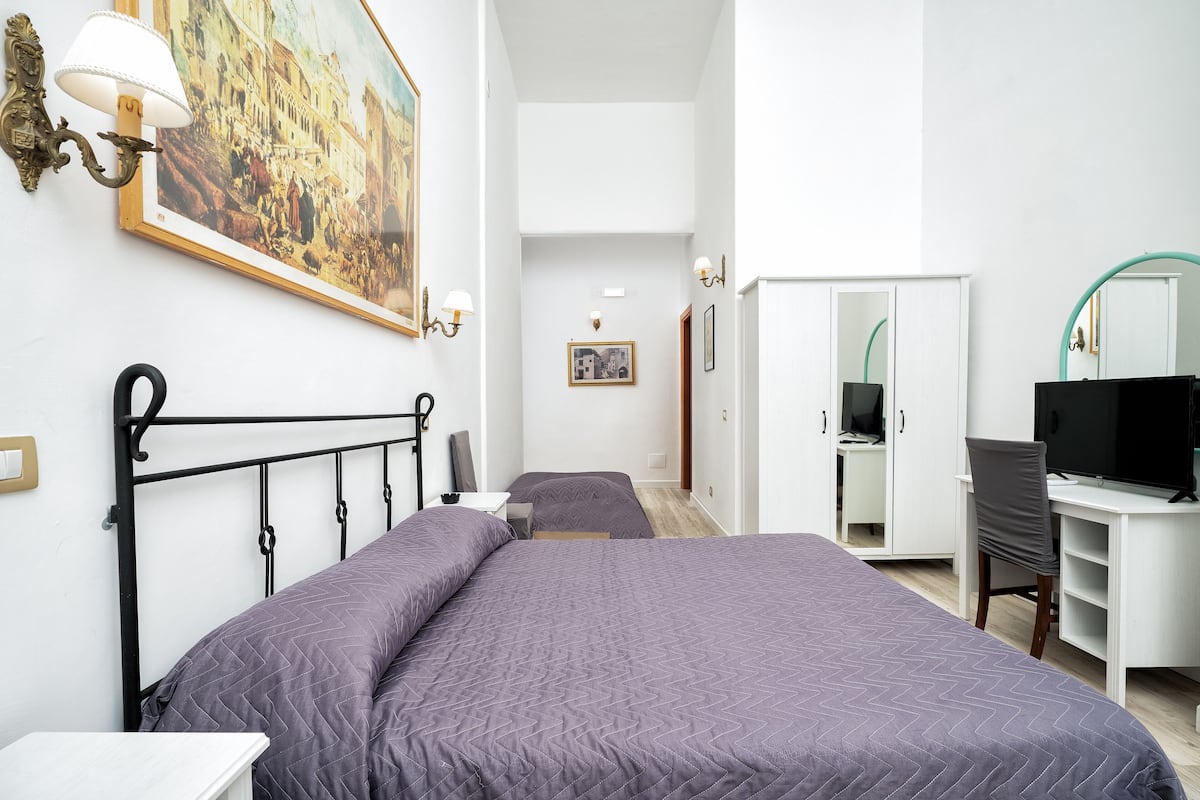 Ein Schlafzimmer mit Bett, Schreibtisch, Stuhl, Fernseher und Kleiderschrank.