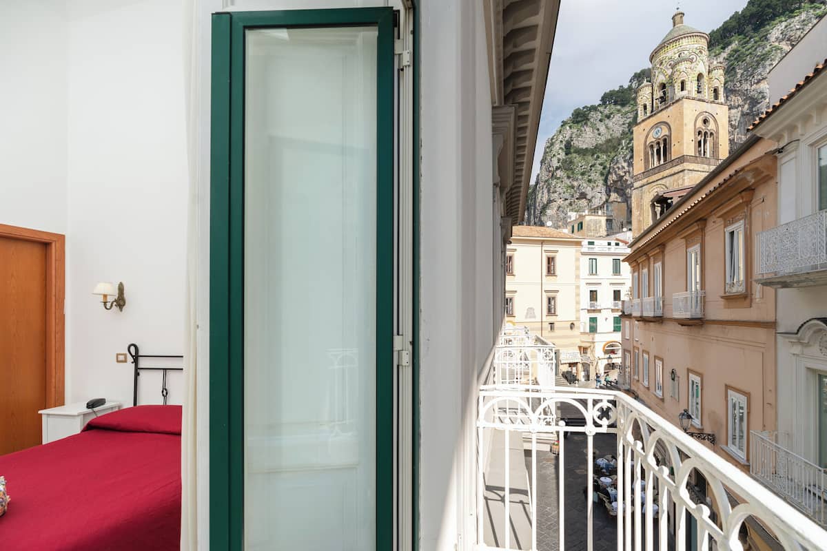Ein Balkon mit weißer Brüstung, der auf eine Straße mit Gebäuden und einem Berg im Hintergrund blickt.