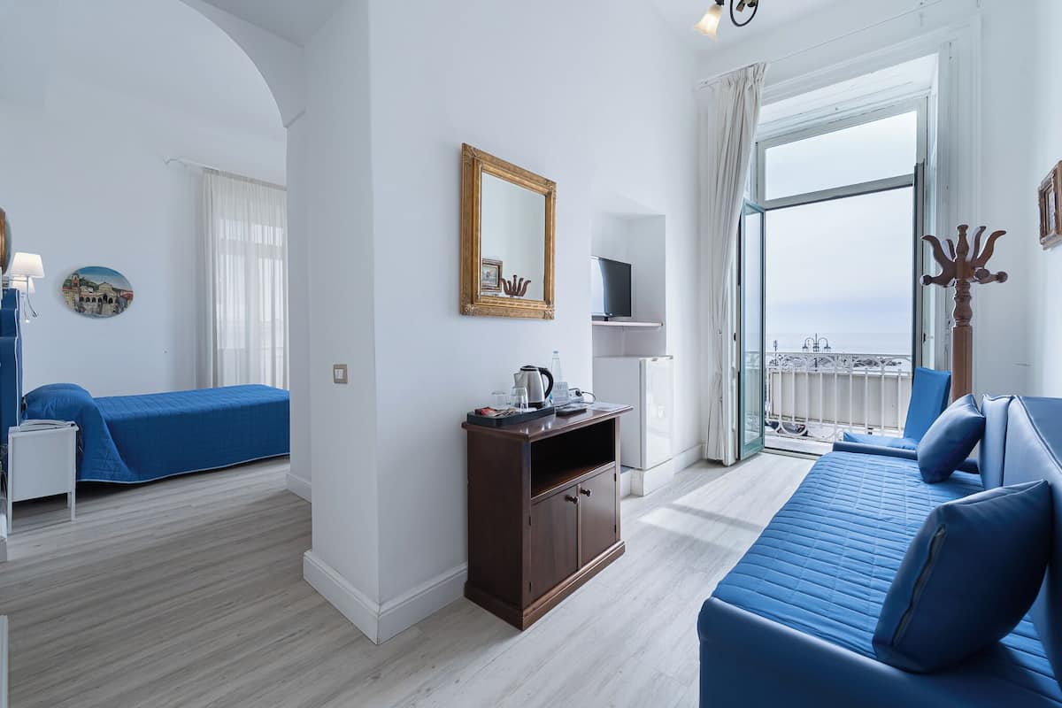 Ein modernes Hotelzimmer mit Balkon, einem Bett, einer Couch und einem kleinen Holzschrank.