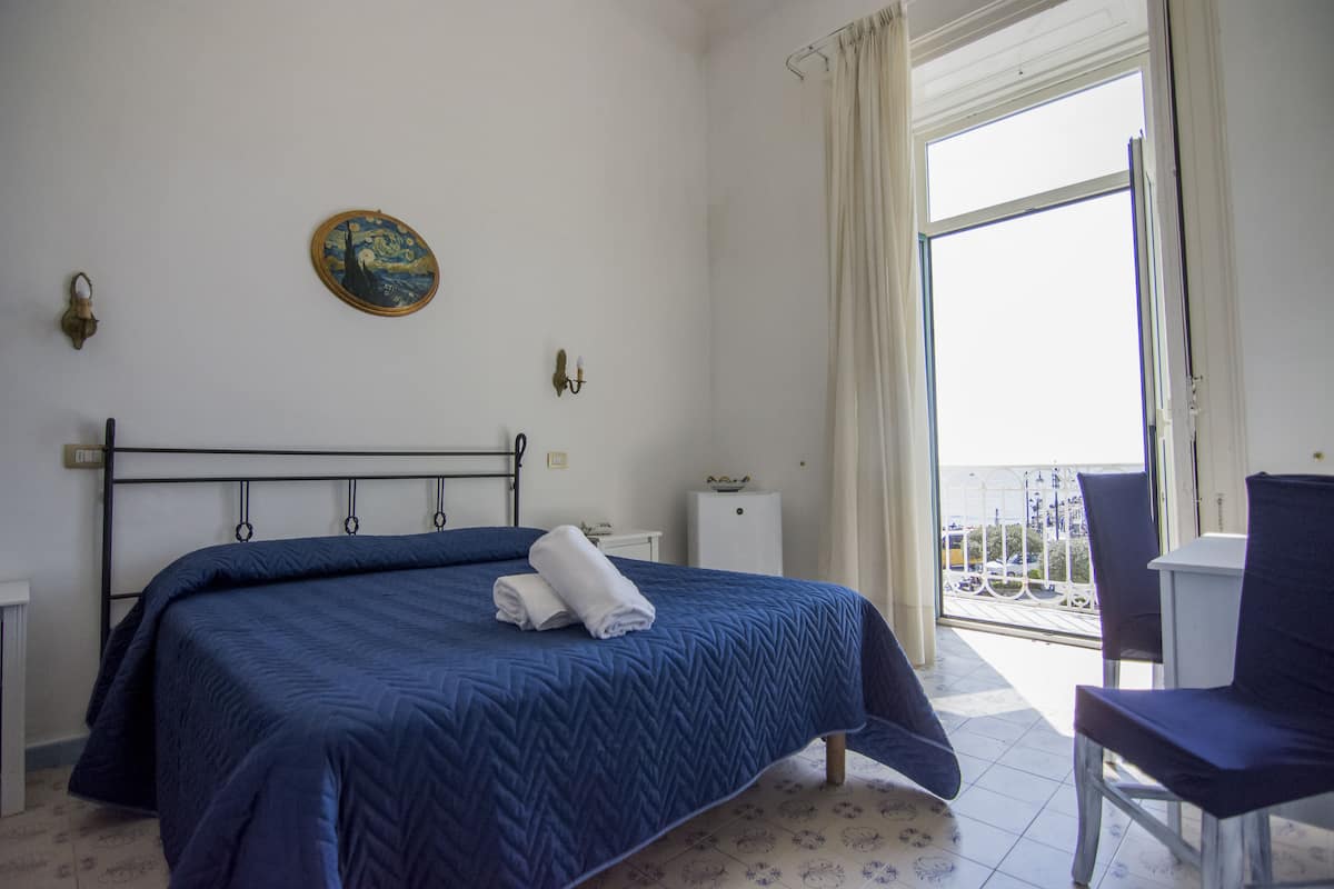 Ein Schlafzimmer mit einem Bett, einem Nachttisch, einem Sessel und einem Balkon mit Geländer.
