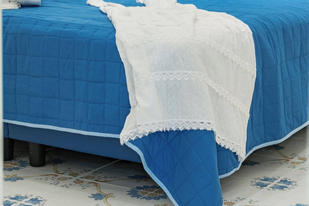 Ein Bett mit blauem Kopfteil und einer weißen Spitzendecke.