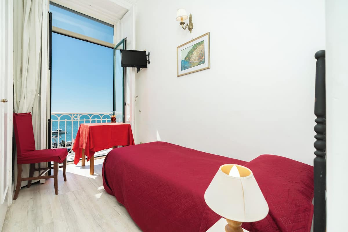 Ein Zimmer mit Bett, Stuhl, Tisch und einem Balkon mit Blick.
