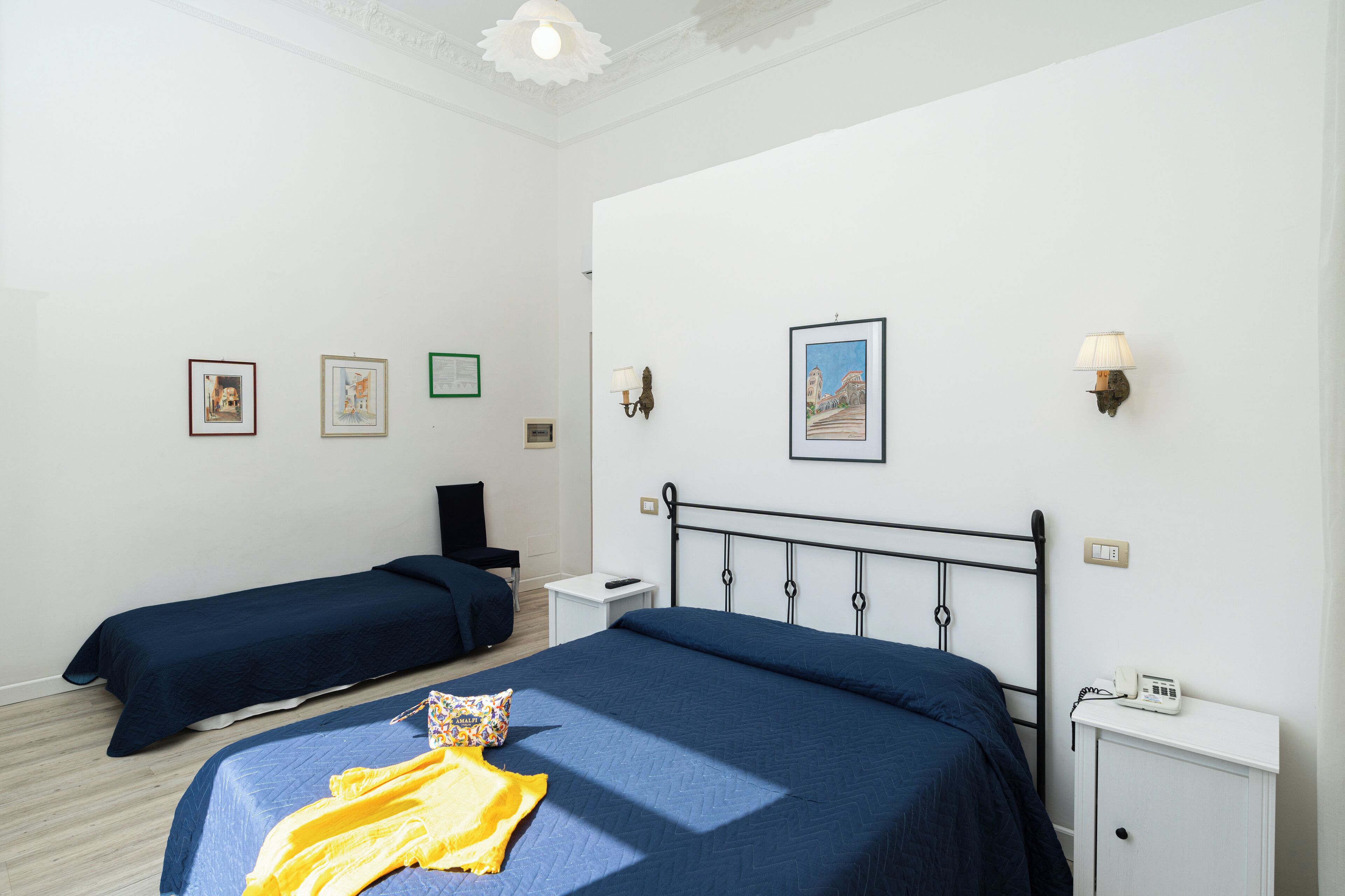 A hotel room with two single beds, a bedside table with a lamp, a phone, and a small cabinet.