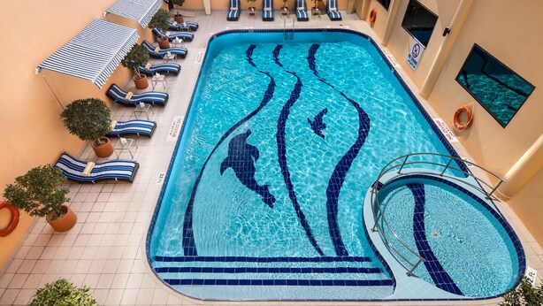 An indoor swimming pool with blue and white tiled patterns, lounge chairs, and potted plants.