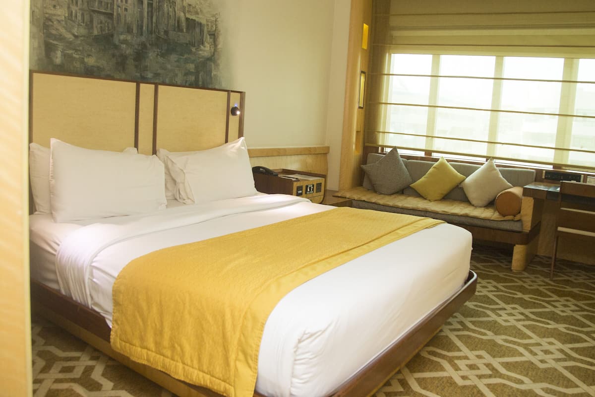 A hotel room with a large bed, a desk, a chair, a window with blinds, and a painting on the wall.