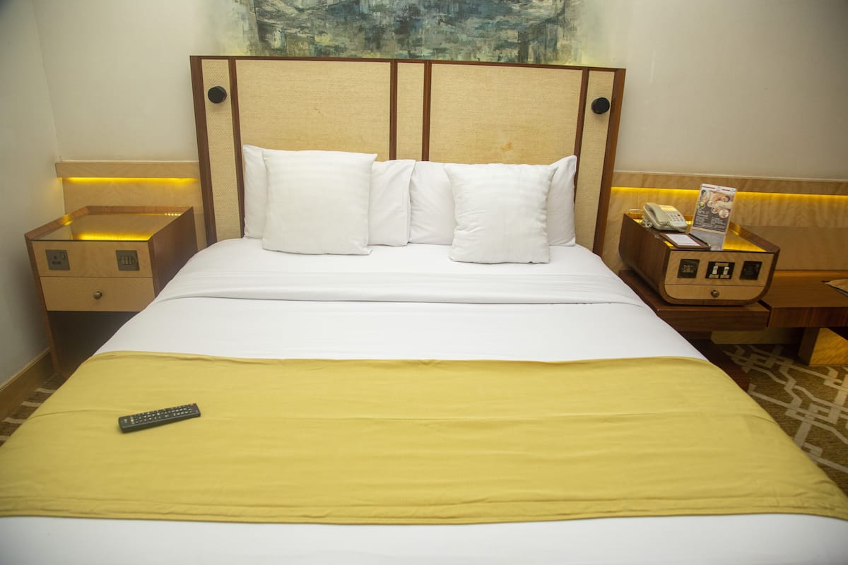 A hotel room with a large bed, a bedside table with a lamp, and a nightstand with a phone and a magazine.