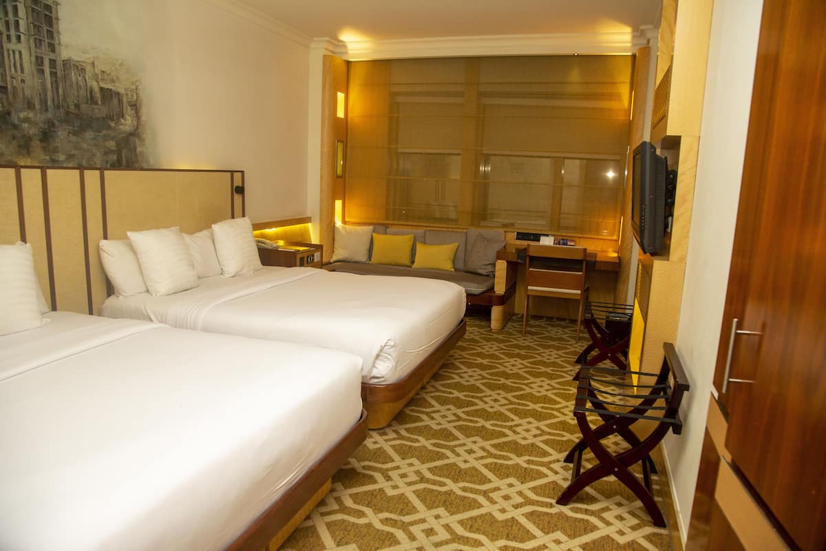 A hotel room with two beds, a desk, a chair, a television, and a large window.