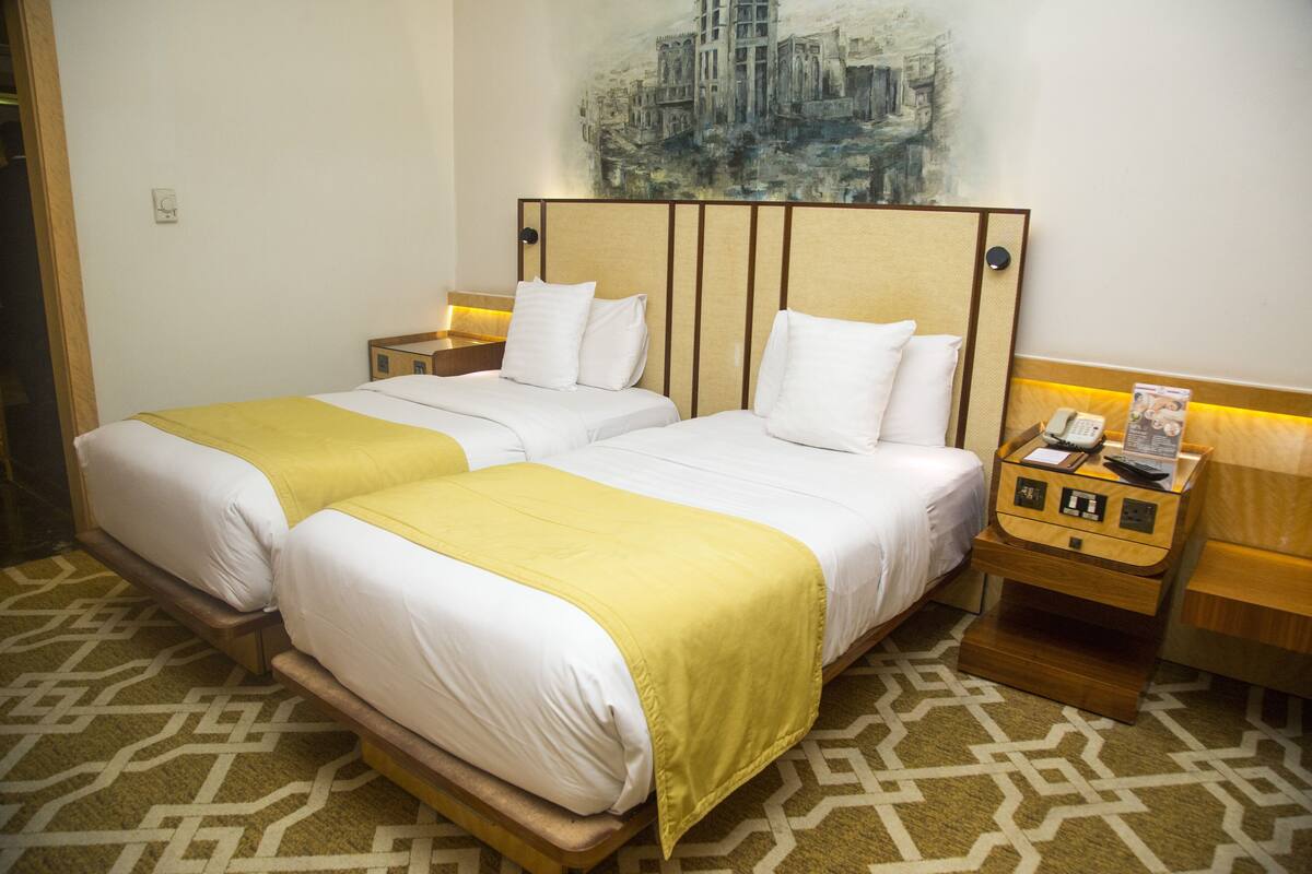 A double bed with a yellow throw, two bedside tables with lamps, and a painting on the wall.