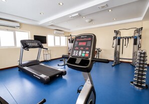 Une salle de sport équipée de divers appareils, notamment un tapis de course, un vélo d’appartement et des appareils de musculation.