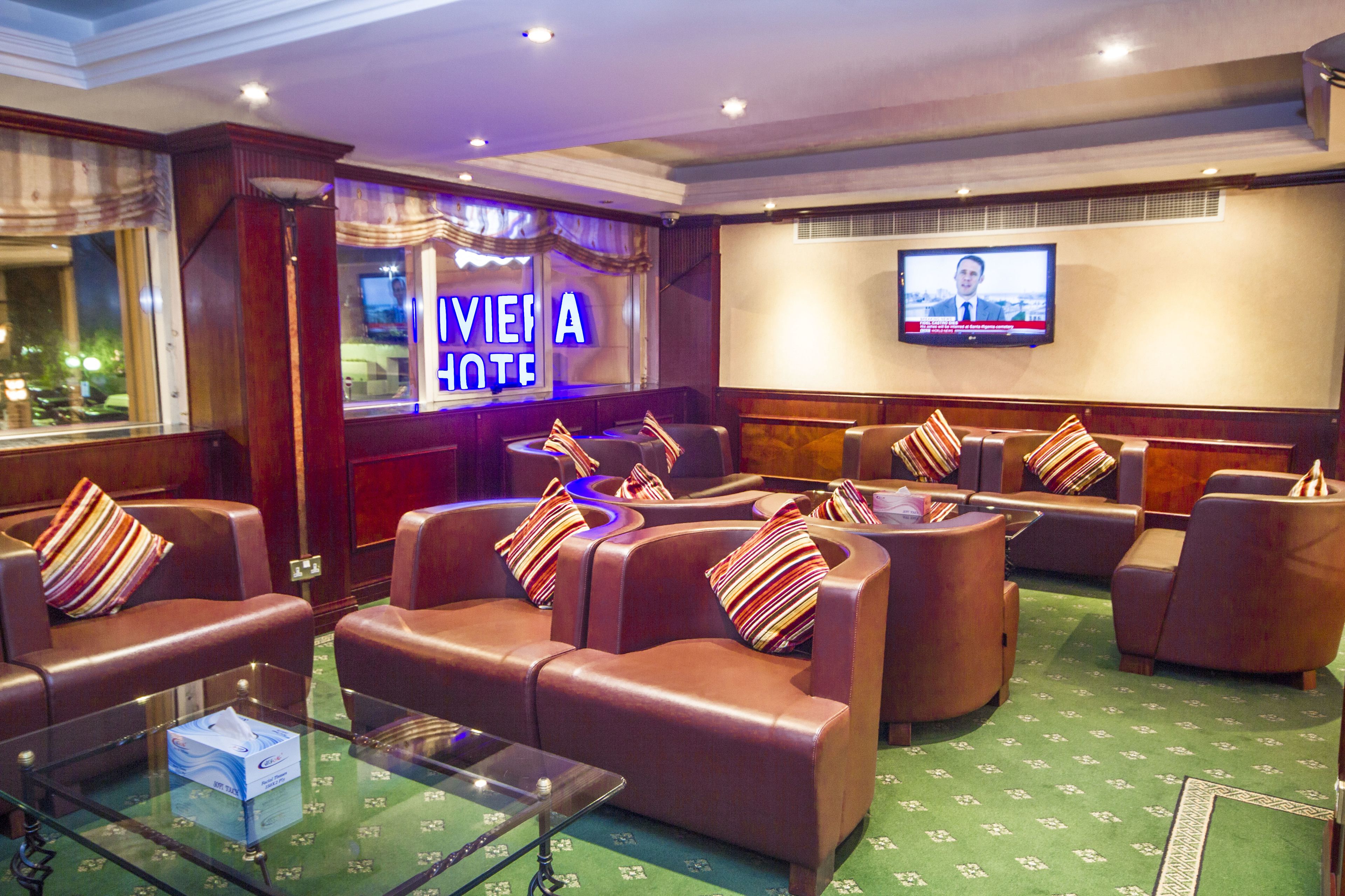 A hotel lobby with leather seating, a glass coffee table, and a television screen.
