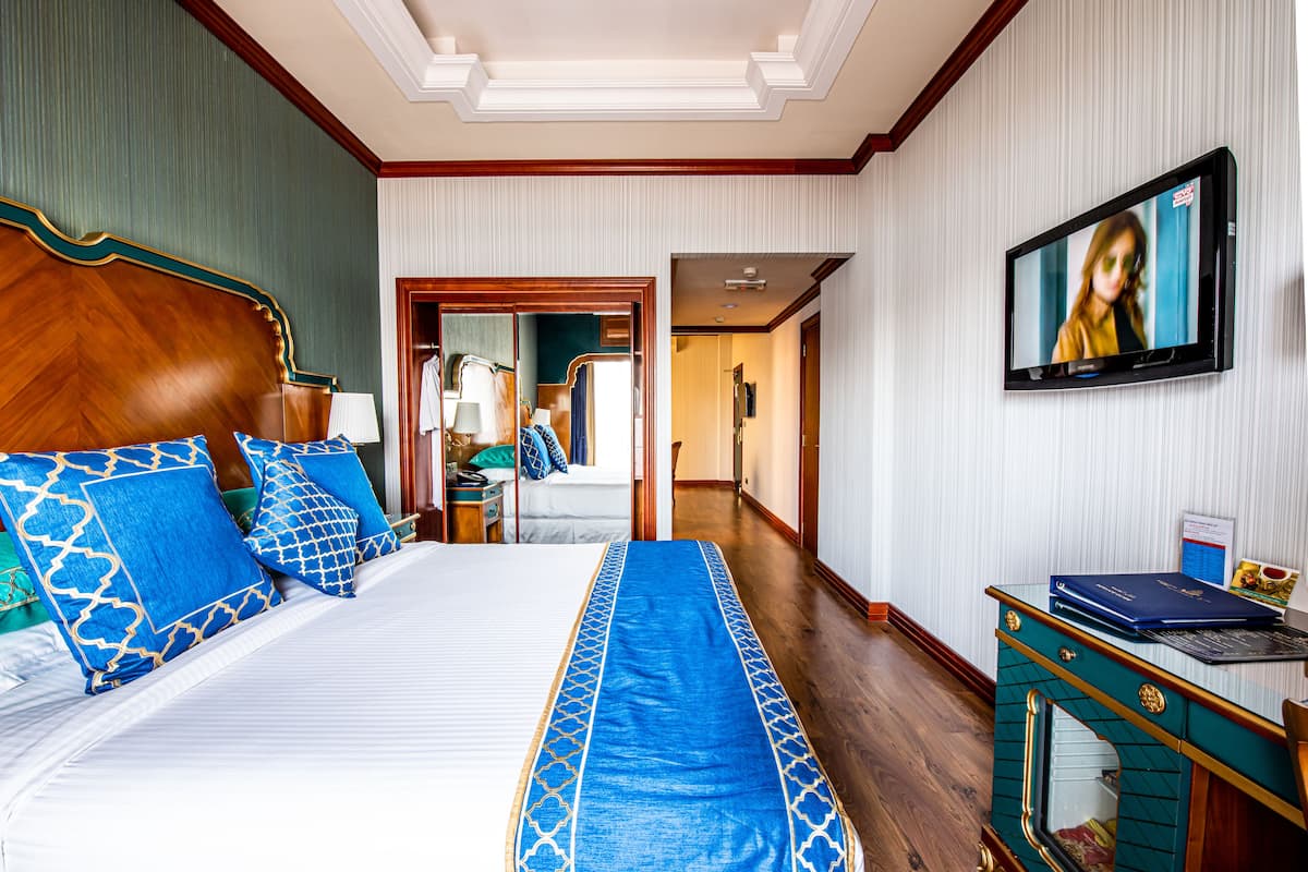 Una habitación de hotel con una cama grande, un televisor montado en la pared y un escritorio con una computadora portátil.