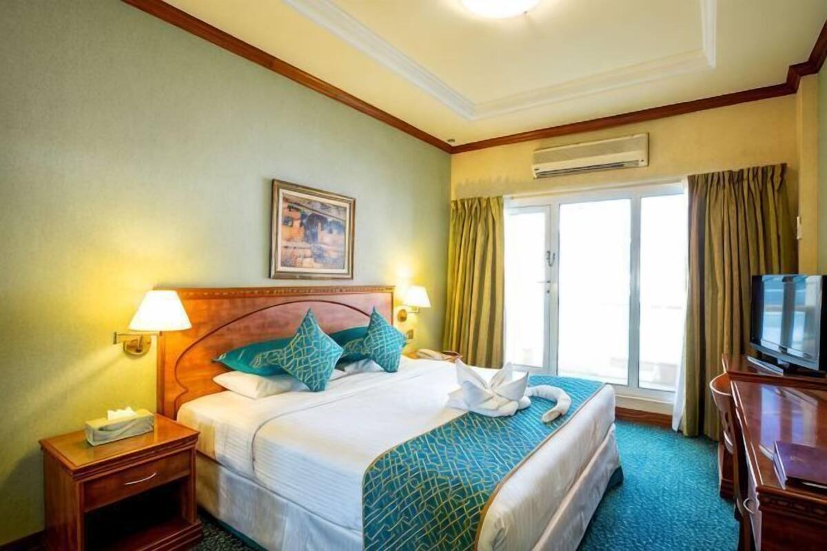 Una habitación de hotel con una cama, una mesita de noche, un televisor y una ventana con cortinas.