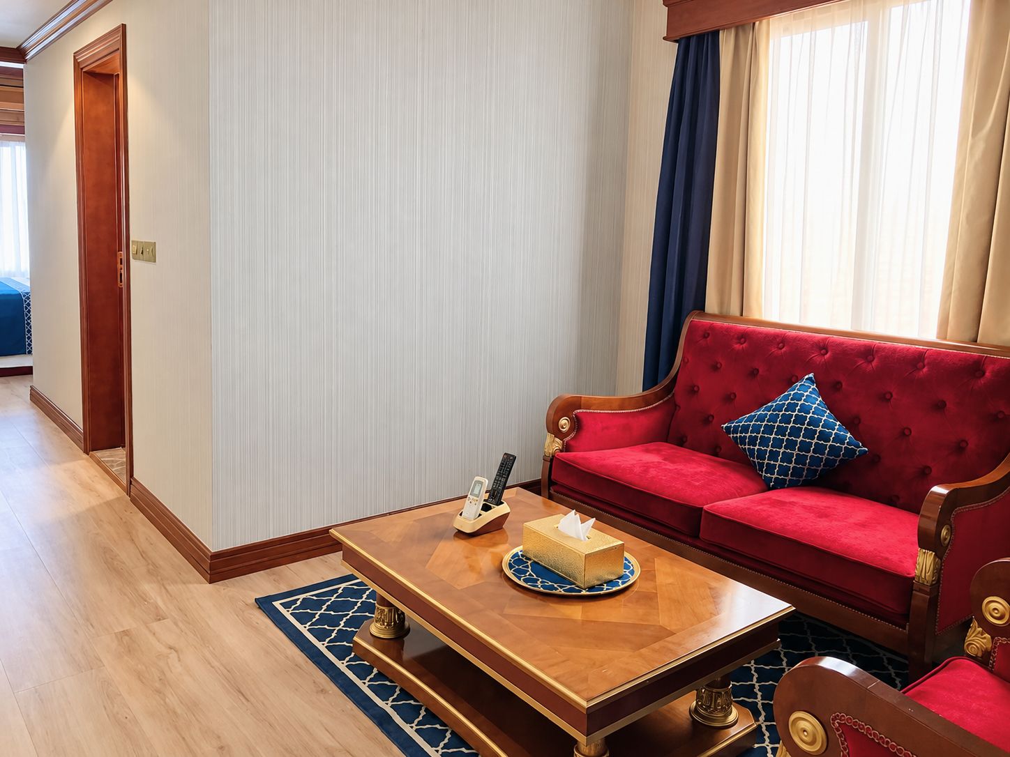 A hotel room with a red sofa, a wooden coffee table, and a blue patterned rug.