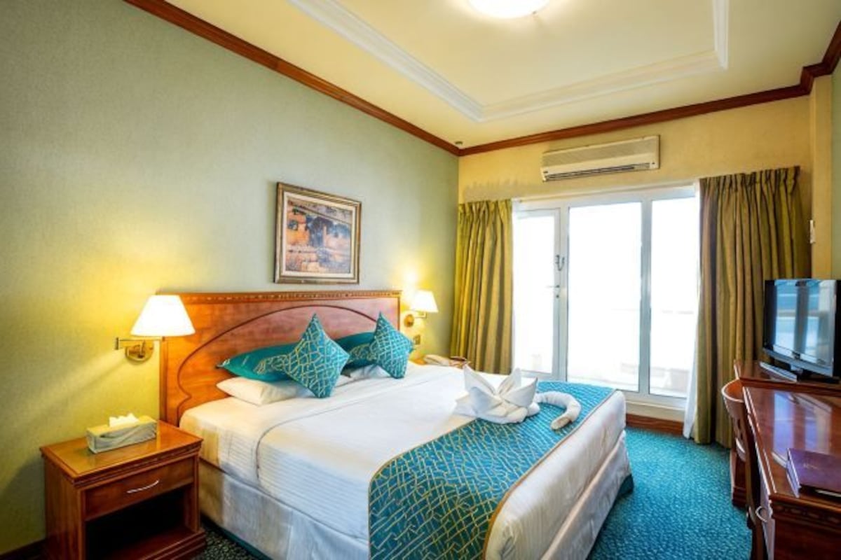A hotel room with a bed, a nightstand, a television, and a window with curtains.