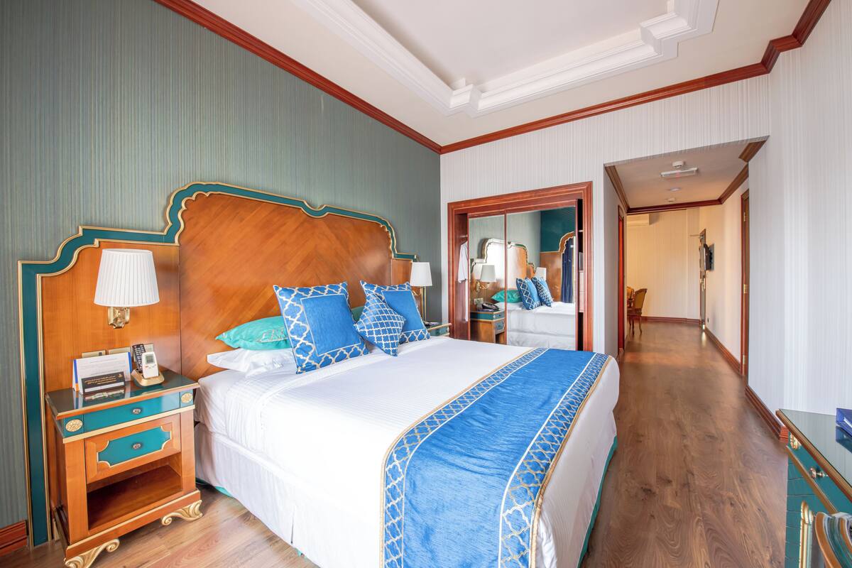 Habitación de hotel con una cama grande, una mesita de noche de madera con una lámpara y un espejo sobre la cama.