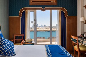 A hotel room with a bed, a chair, a table, and a view of a cityscape and water. - Riviera Hotel Dubai (Dubai)