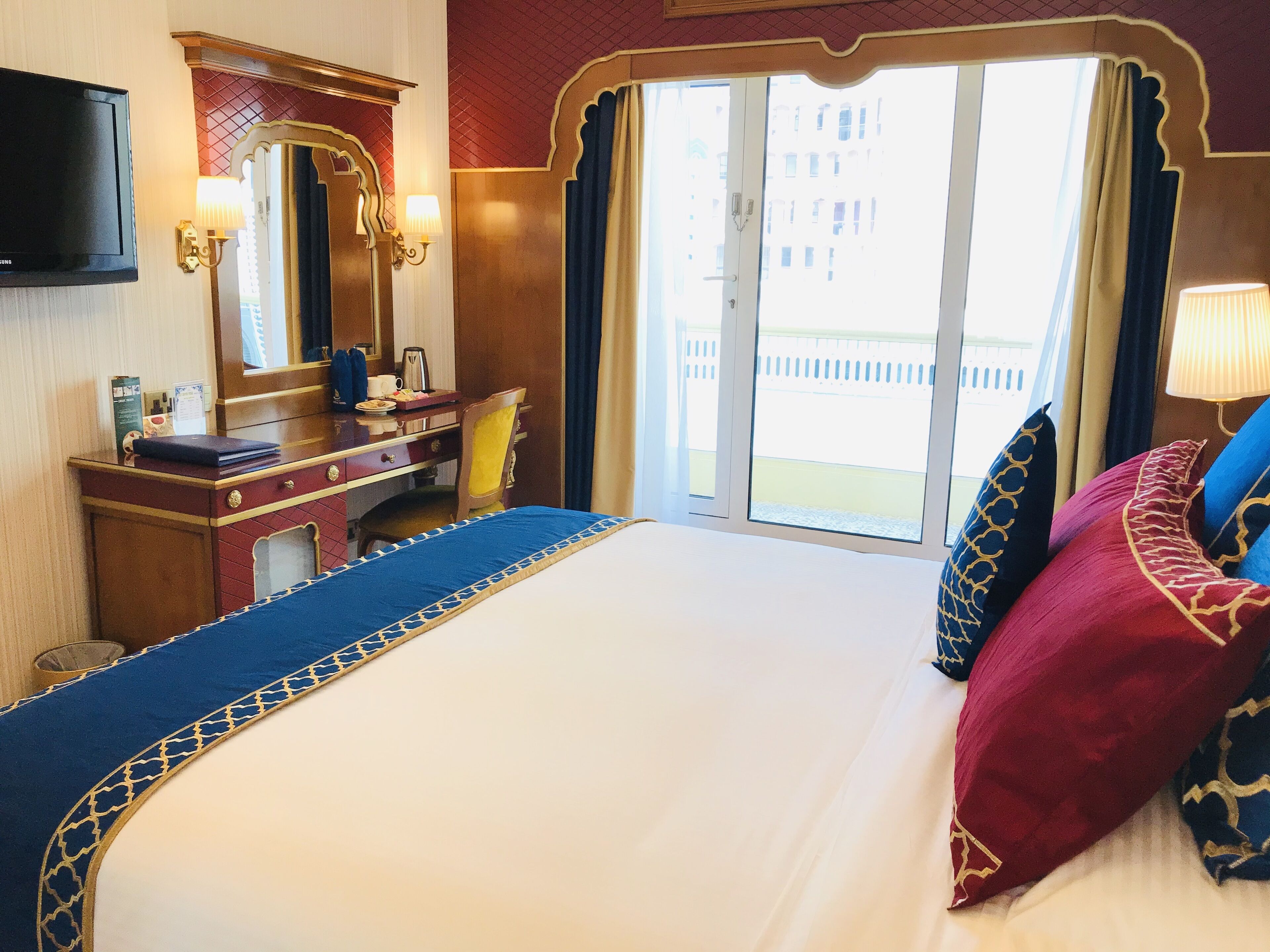 A hotel room with a large bed, a desk with a chair, a flat-screen TV, and a window with curtains.