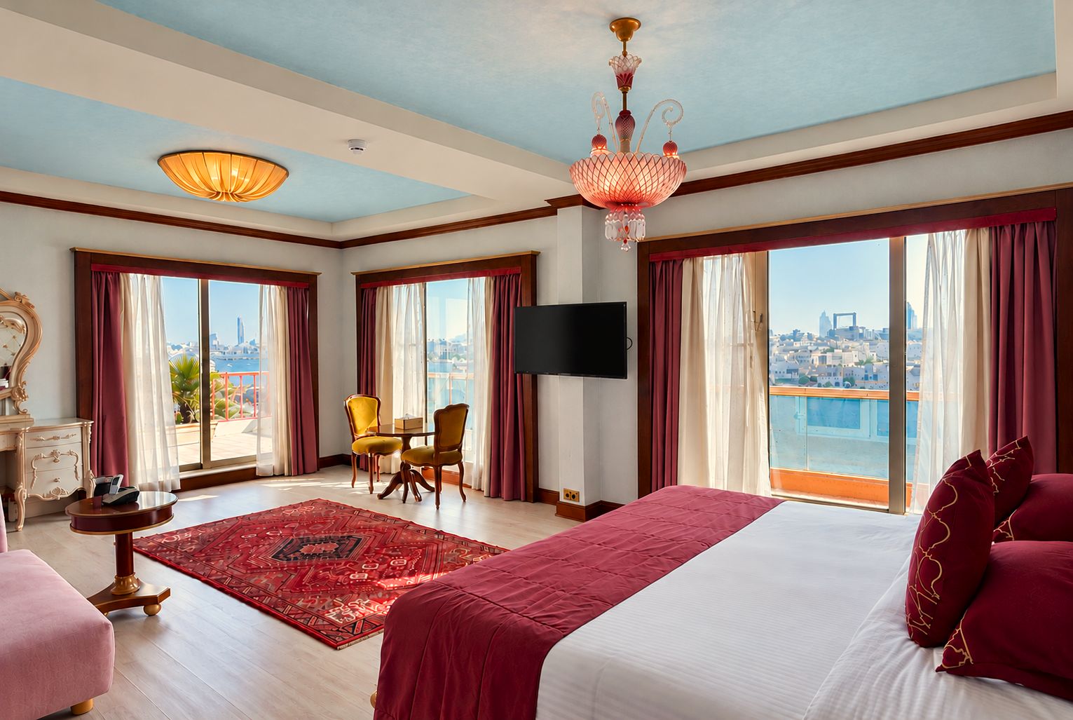 Une chambre d’hôtel avec un grand lit, une télévision, un coin repas avec des chaises et une vue sur la ville.