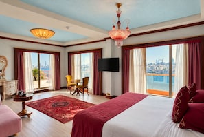 A hotel room with a large bed, a television, a dining area with chairs, and a view of the city. - Riviera Hotel Dubai (Dubai)