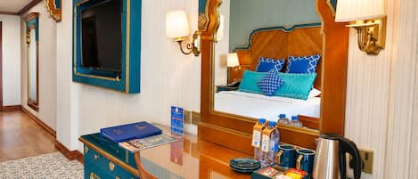 Habitación de hotel con un espejo grande, una cama con almohadas azules, un minibar y un televisor.