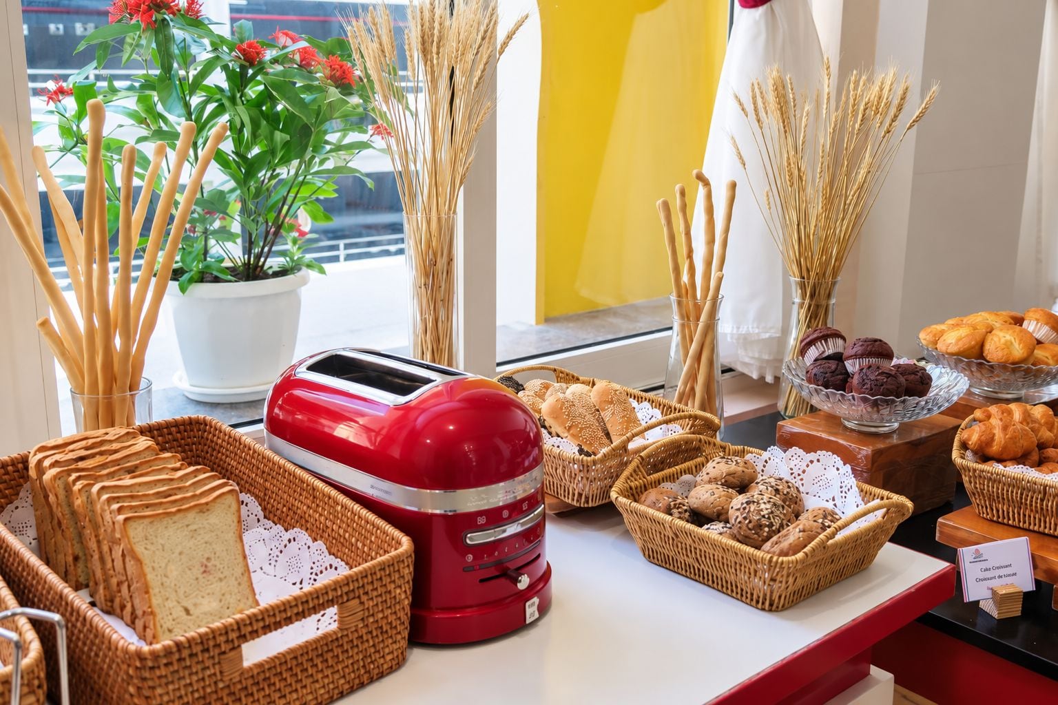 Een ontbijtbuffet met verschillende broden, gebak en een rode broodrooster.