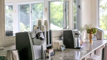 A coffee machine and a beverage dispenser in a well-lit room with large windows.