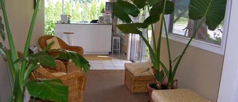 A cozy room with wicker furniture, large potted plants, and a view of the outside.
