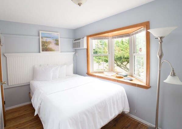 A bedroom with a bed, a window with a view of greenery, a radiator, and a lamp.