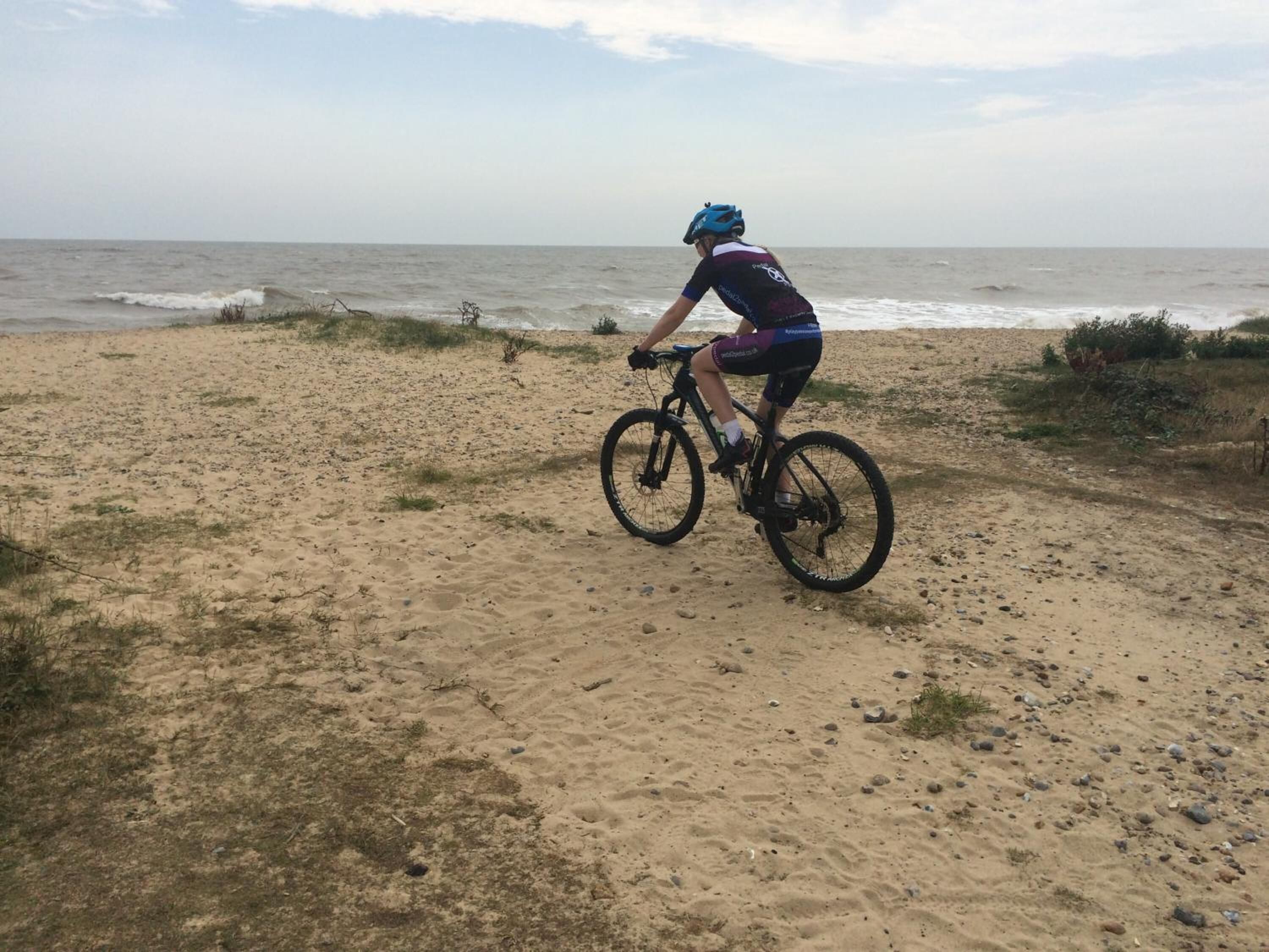 Een zanderig strand met een fietser in helm en fietskleding.