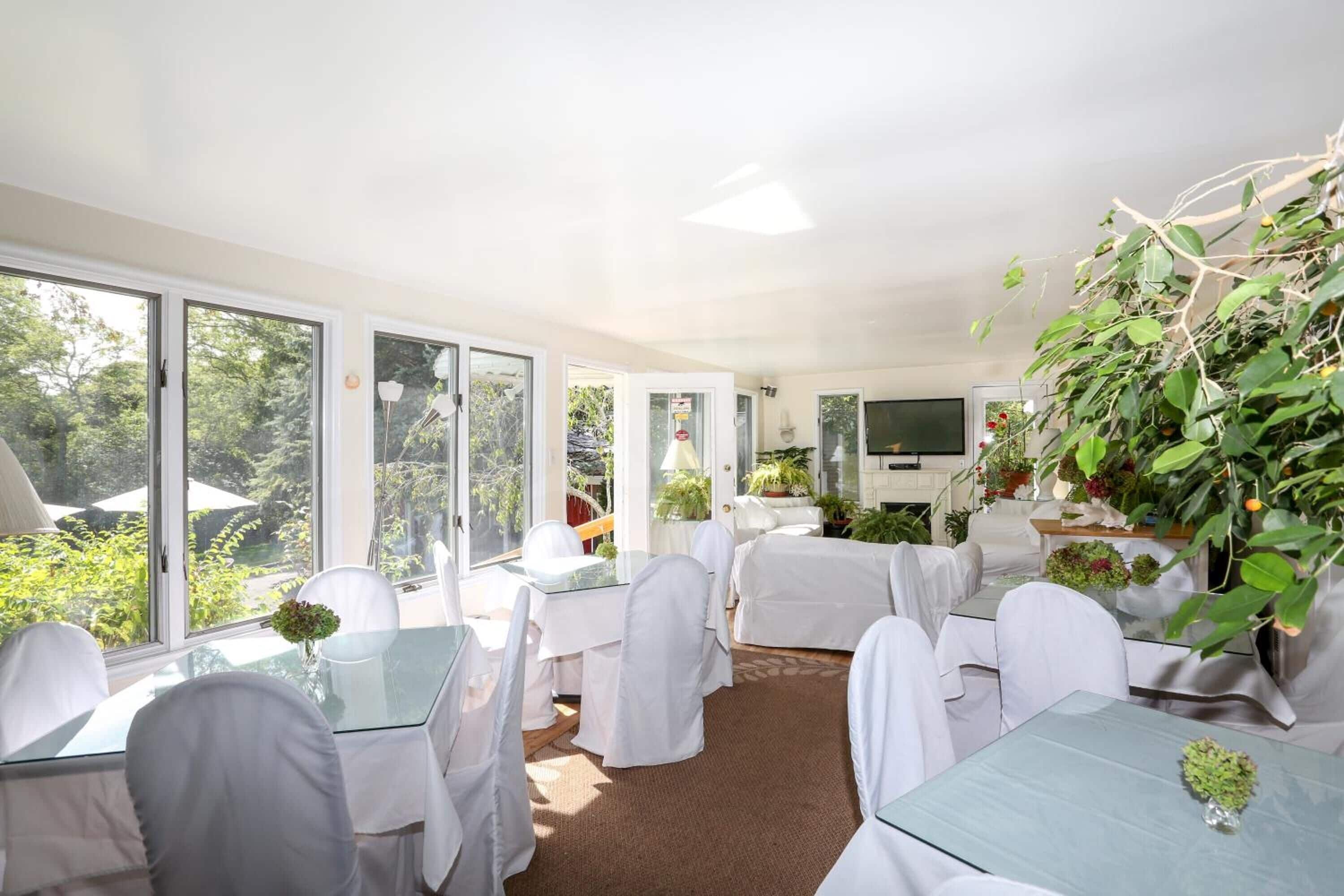 A room with large windows, white chairs, and tables, some with plants.