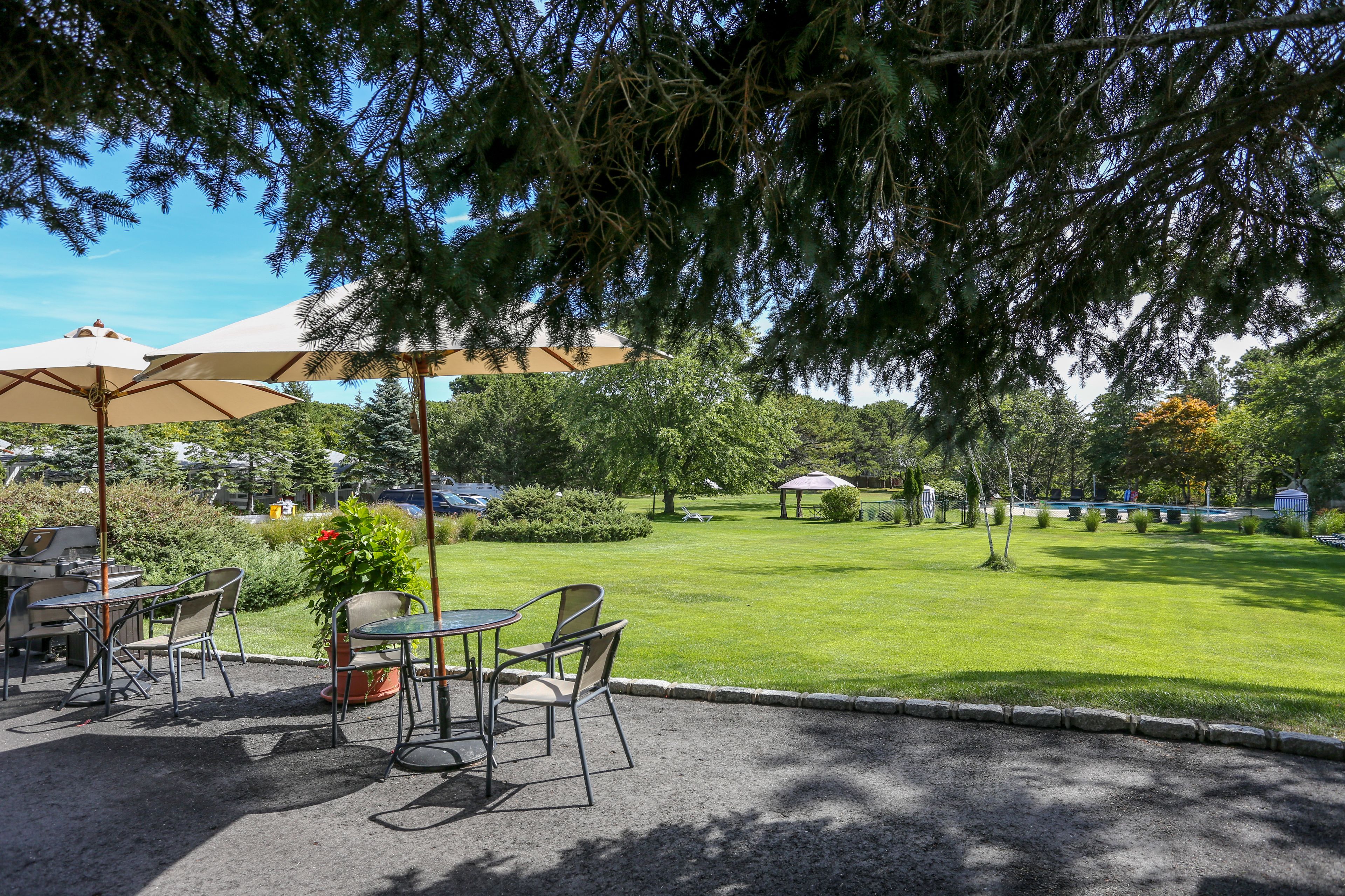 Un espace extérieur aménagé en terrasse, avec des tables et des chaises, une pergola dotée de parasols et une pelouse bien entretenue.
