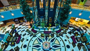 A spacious atrium with a central circular seating area, multiple levels with seating, and a large tree in the center. - Emirates Concorde Hotel & Suites (Dubai)