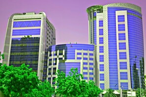 A modern building with a curved facade, large windows, and a prominent logo at the top. - Emirates Concorde Hotel & Suites (Dubai)