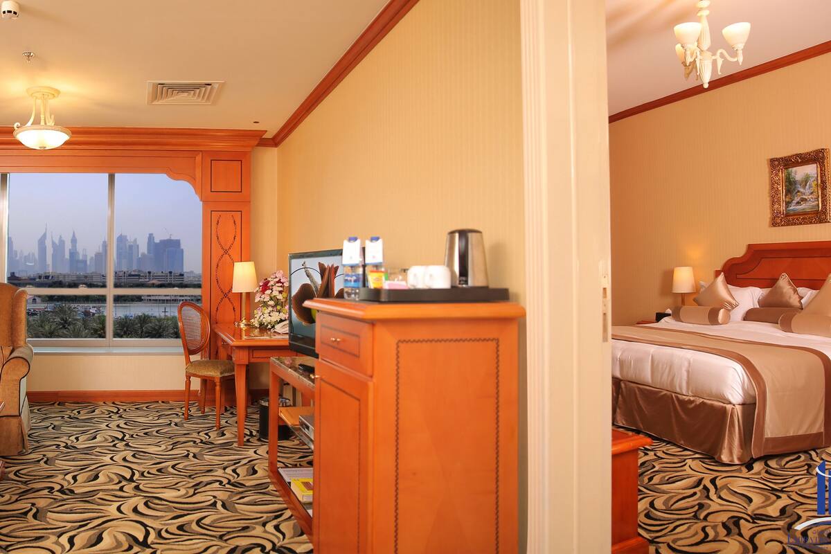 A hotel room with a city view, a bed, a desk, a chair, and a coffee table.