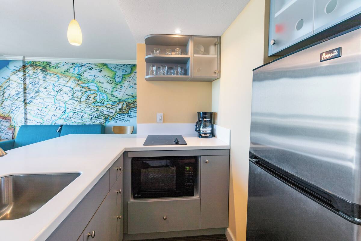 Una cocina compacta con microondas integrado, un refrigerador de acero inoxidable, cafetera y un mapa en la pared.