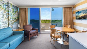 A hotel room with a large window, a map wall, a sofa, a chair, a table, and a painting. - Oceanfront Pan American Hotel (Wildwood Crest)
