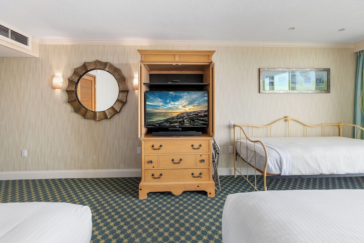 Habitación de hotel con dos camas individuales, un aparador de madera, un televisor de pantalla plana, un espejo redondo y un cuadro en la pared.