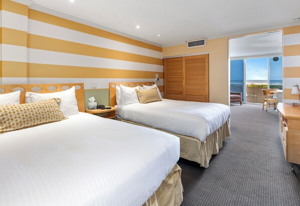 A hotel room with two beds, a desk, and a view of the ocean.