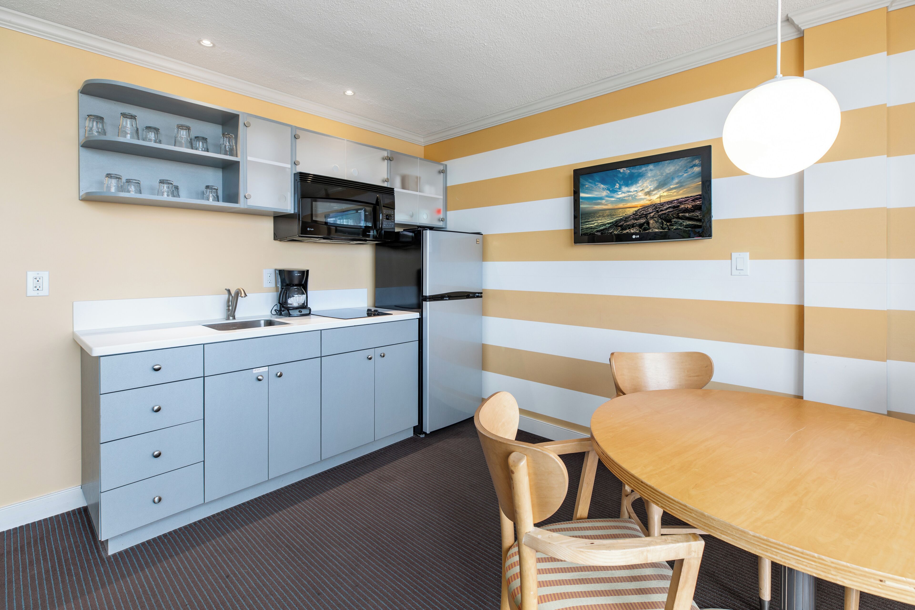 A modern kitchen with grey cabinets, a stainless steel refrigerator, and a wooden dining table with chairs.