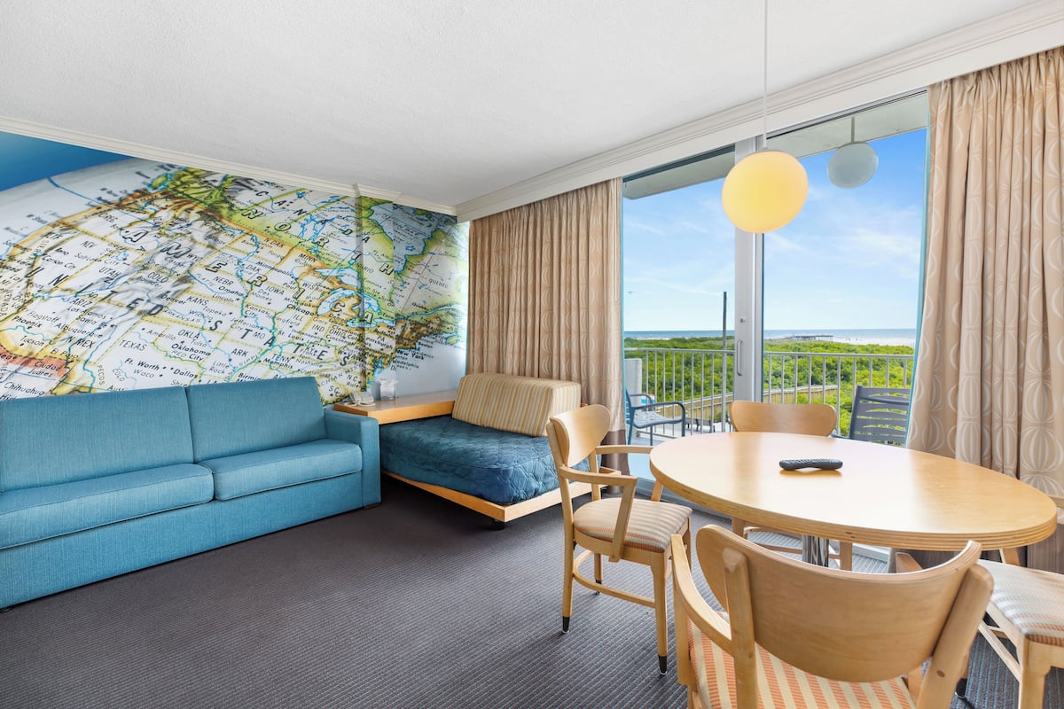 Una habitación con un sofá azul, un mural de mapa, una mesa de comedor con sillas y vistas al exterior.