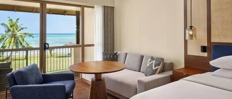 A hotel room with a balcony, a round wooden table, a sofa, a bed, and a hanging light fixture.