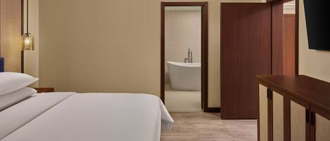 Habitación de hotel con cama, tocador de madera, televisor y baño con bañera.