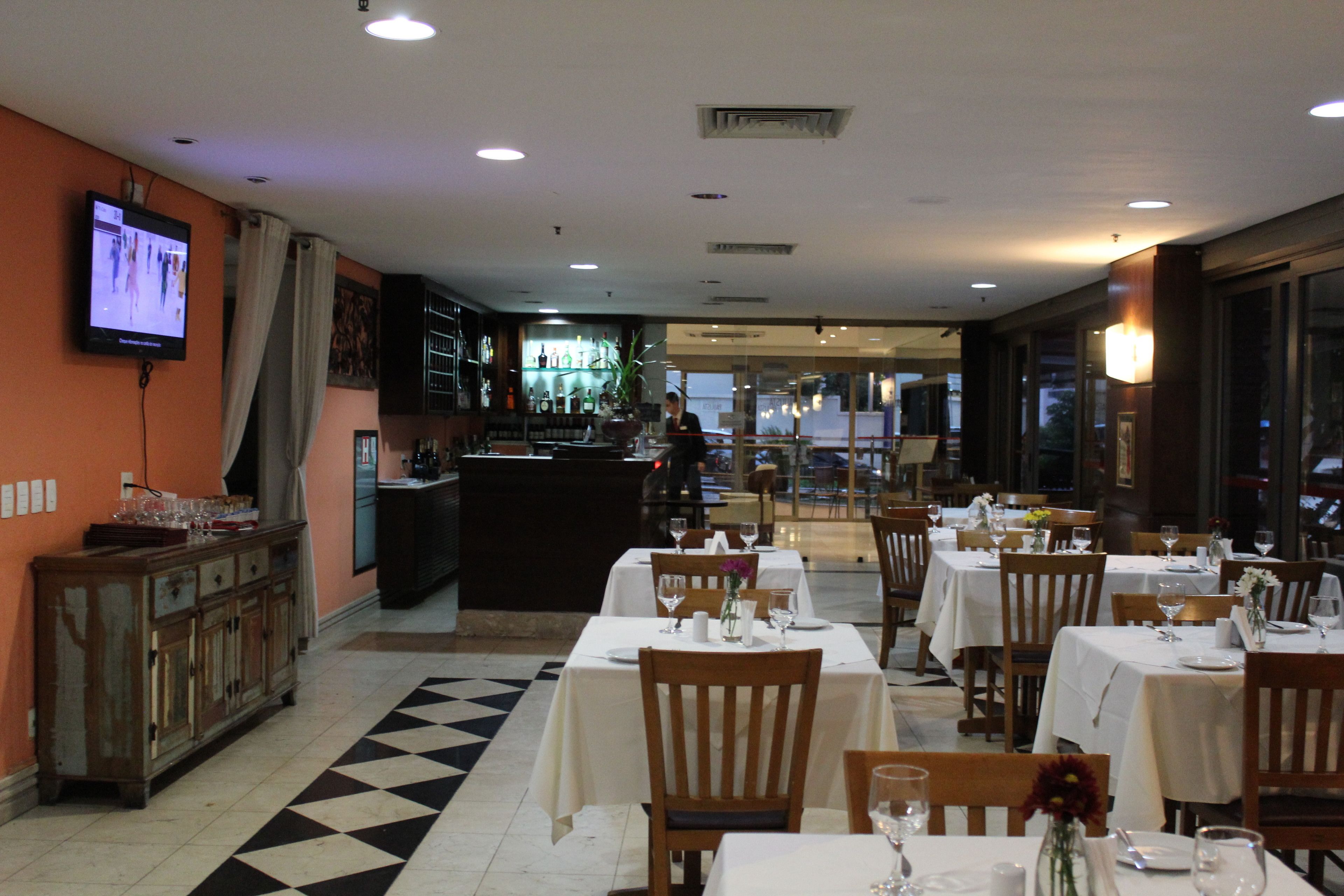 Un restaurante con varias mesas y sillas, una zona de bar y una pantalla de televisión mostrando un evento deportivo.
