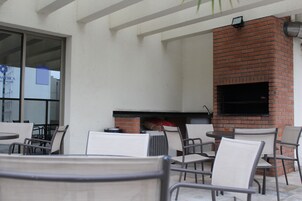 An outdoor patio with brick fireplace, white chairs, and tables.