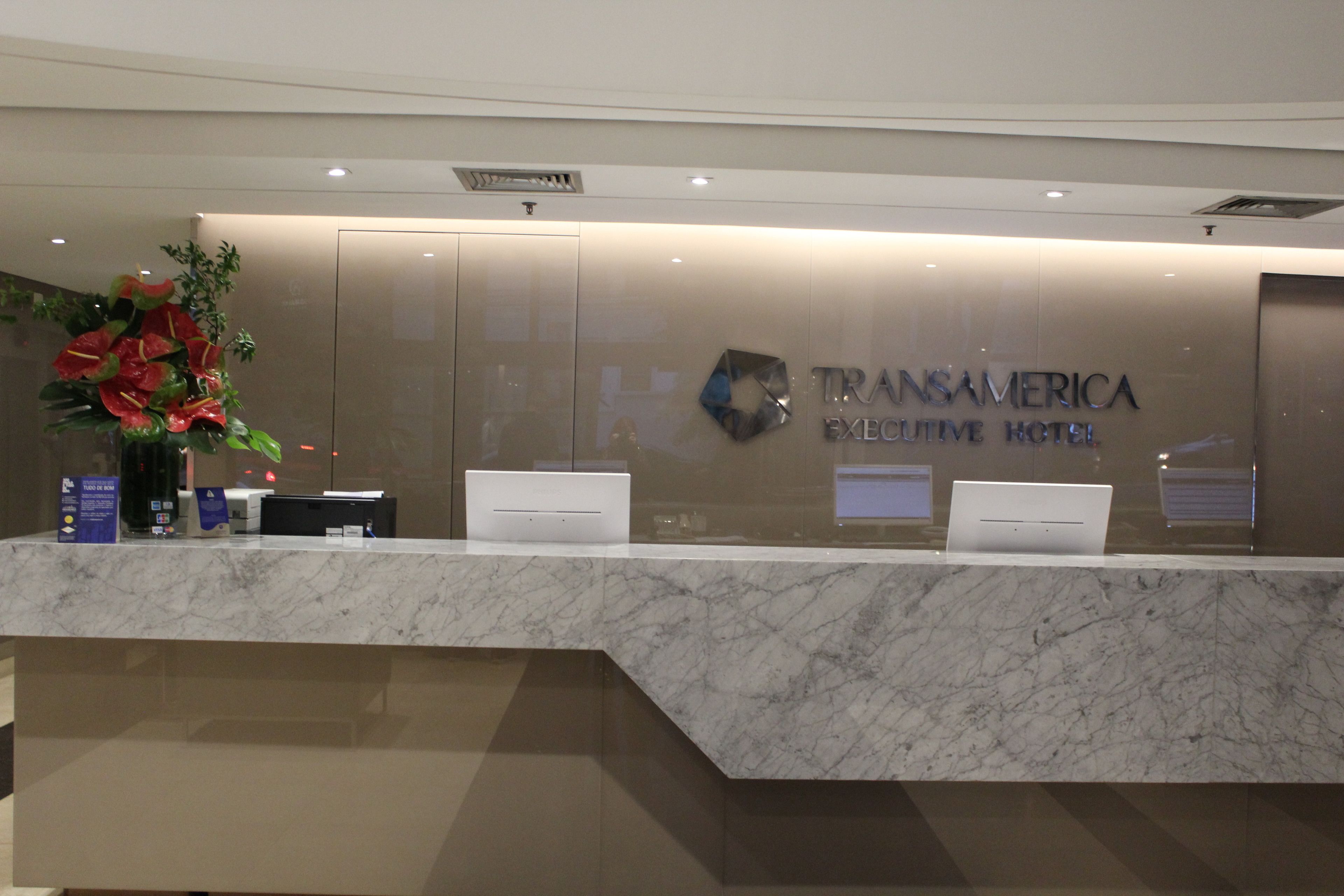 Una recepción con encimera de mármol, dos computadoras portátiles y un cartel para el Hotel Ejecutivo Transamerica.