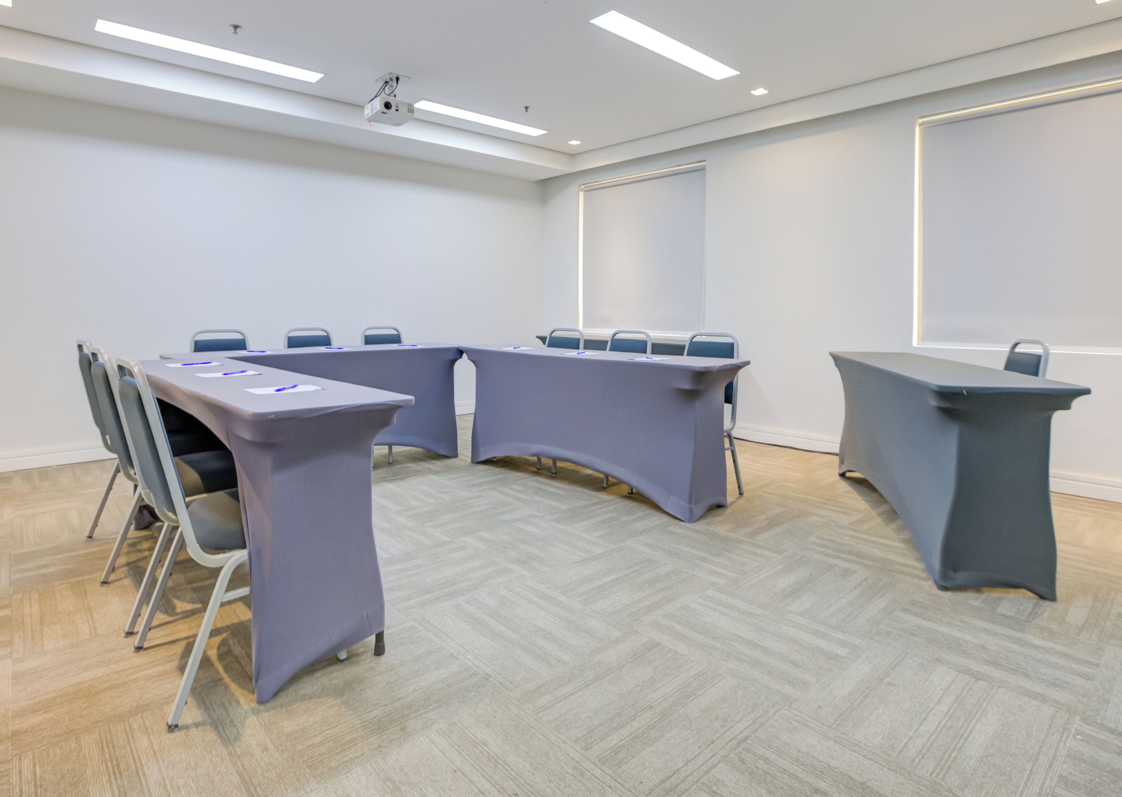 A conference room with a U-shaped table, chairs, and a projector on the ceiling.